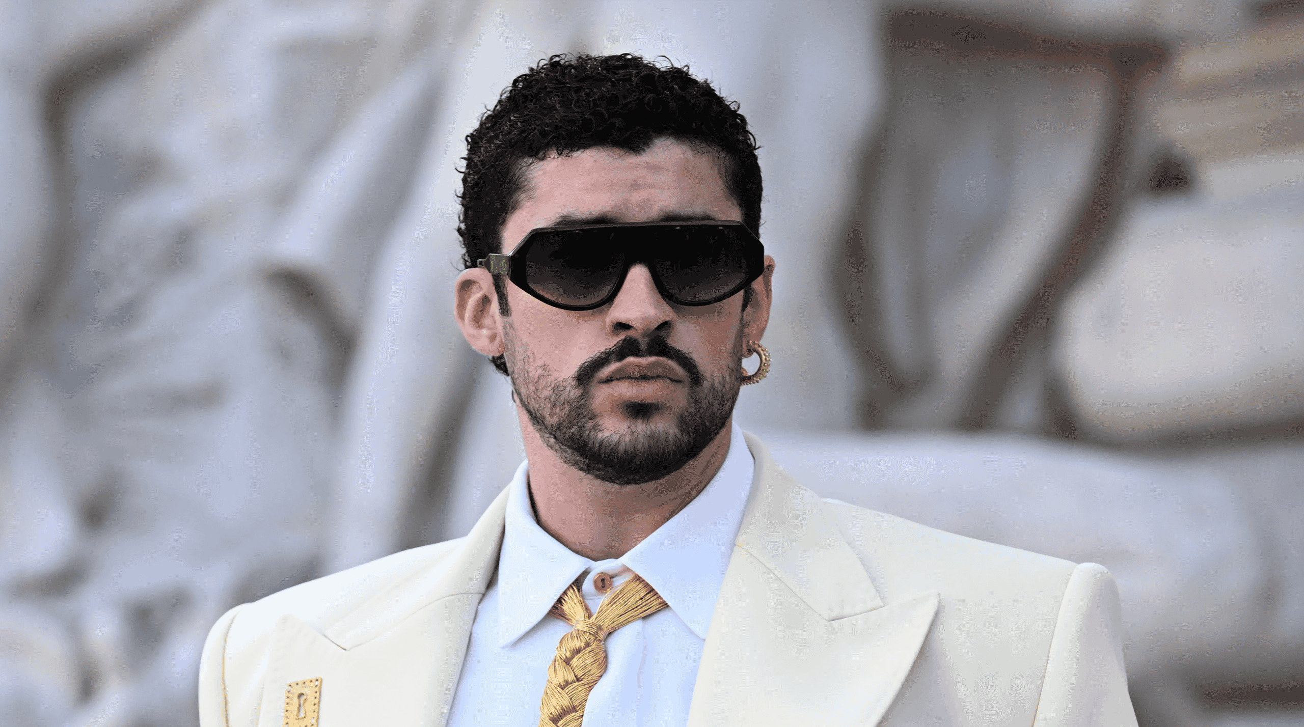 Bad Bunny in a cream suit wearing sunglasses.